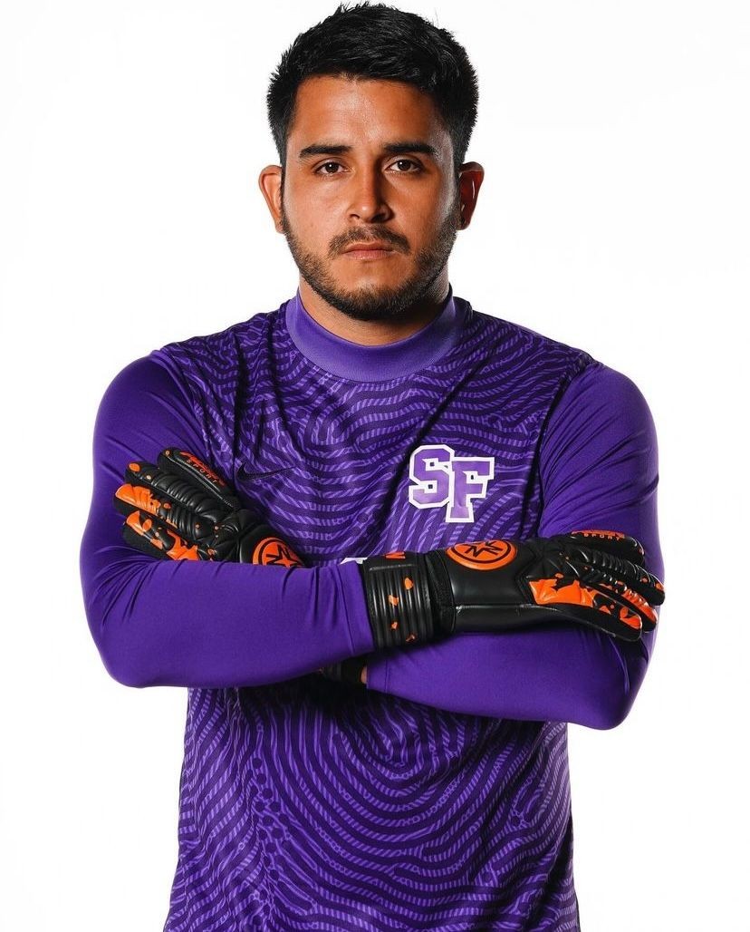 Person wearing a purple sports jersey with crossed arms, featuring black and orange gloves.